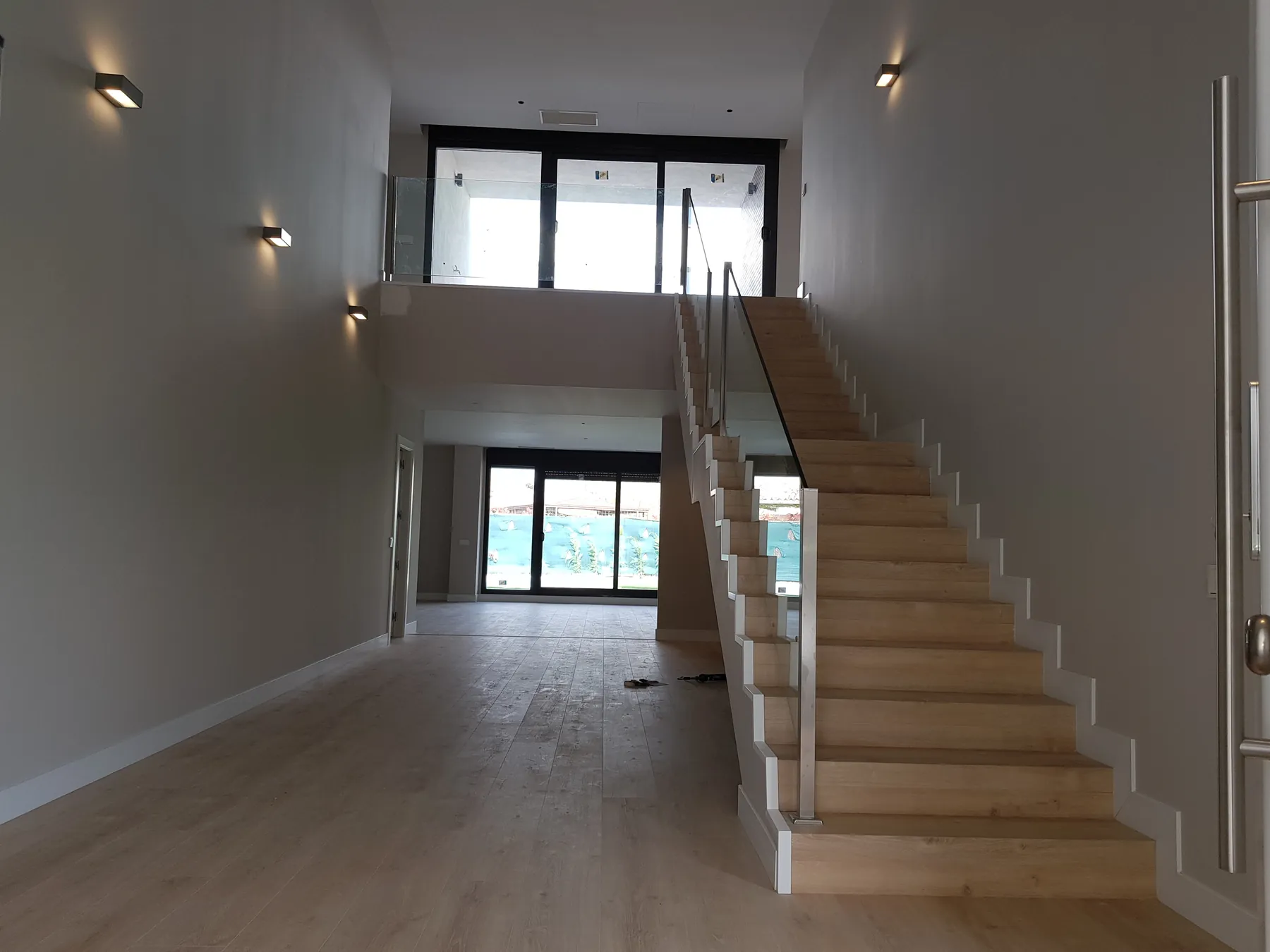 Recibidor a doble altura con escalera de madera y cristal